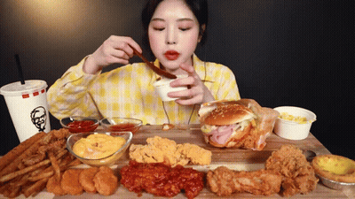 A Woman In A Yellow Plaid Shirt Is Eating A Kfc Hamburger And French Fries GIF