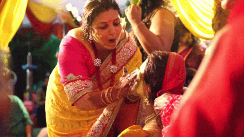 A Woman In A Yellow Sari Is Applying Powder To Another Woman 'S Face . GIF