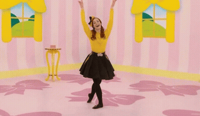 A Woman In A Yellow Shirt And Black Skirt Is Dancing In A Pink Room GIF