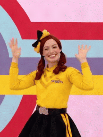 A Woman In A Yellow Shirt And Black Skirt Is Standing In Front Of A Colorful Background . GIF
