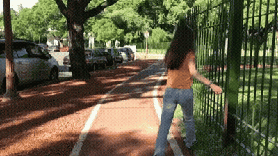 A Woman In A Yellow Shirt And Blue Jeans Is Walking Down A Bike Path GIF