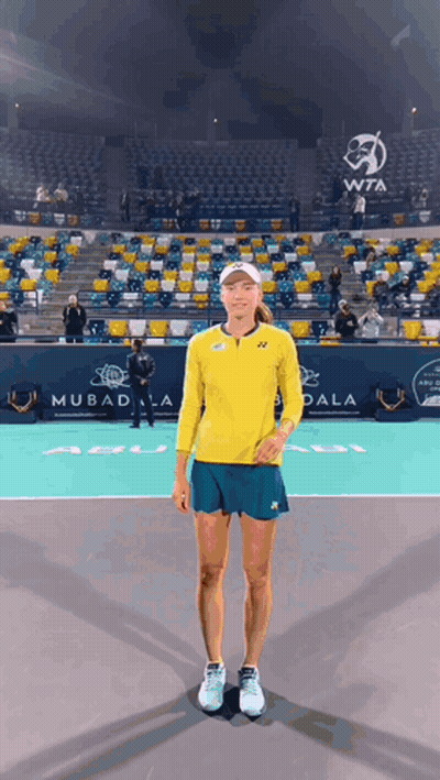 A Woman In A Yellow Shirt And Blue Shorts Is Standing On A Tennis Court GIF