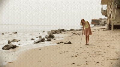 A Woman In A Yellow Shirt And Pink Skirt Is Walking Along The Beach GIF
