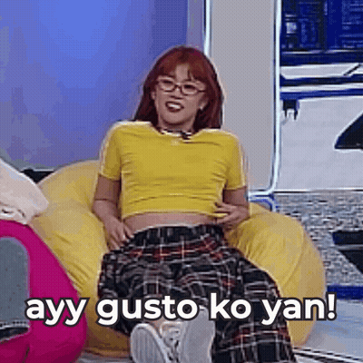 A Woman In A Yellow Shirt And Plaid Pants Is Sitting On A Bean Bag Chair With Her Legs Crossed . GIF