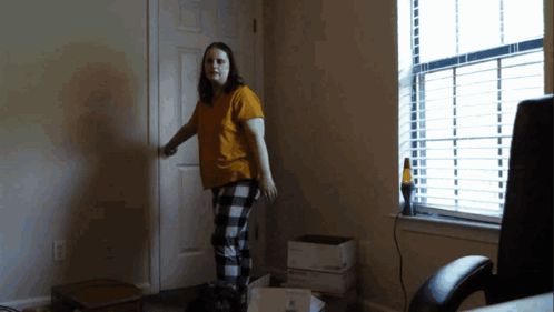 A Woman In A Yellow Shirt And Plaid Pants Is Standing In A Dark Room GIF