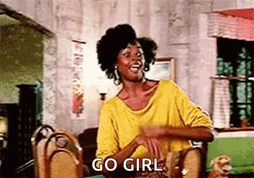 A Woman In A Yellow Shirt Is Sitting At A Table And Says Go Girl GIF