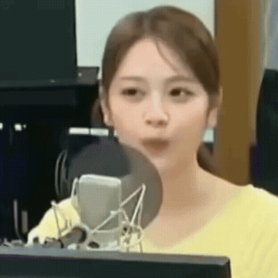 A Woman In A Yellow Shirt Is Sitting In Front Of A Microphone . GIF