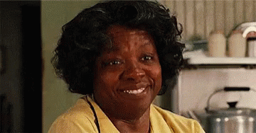 A Woman In A Yellow Shirt Is Smiling And Looking At The Camera In A Kitchen . GIF