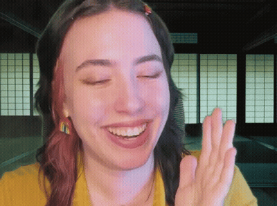 A Woman In A Yellow Shirt Is Smiling And Making A Peace Sign GIF