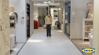 A Woman In A Yellow Shirt Is Walking Down A Hallway With An Ikea Logo On The Floor GIF