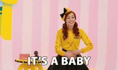 A Woman In A Yellow Shirt With The Words It 'S A Baby On The Bottom GIF