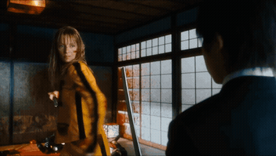 A Woman In A Yellow Suit Is Holding A Gun GIF