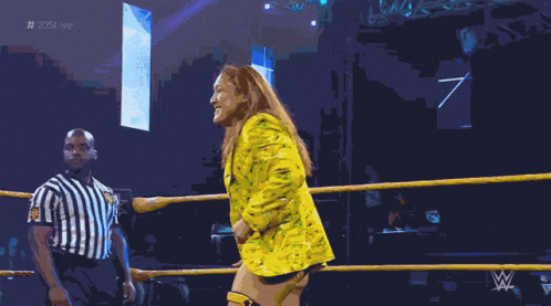 A Woman In A Yellow Suit Is Standing In A Wrestling Ring With A Referee GIF