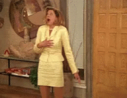 A Woman In A Yellow Suit Is Standing In Front Of A Wooden Door GIF