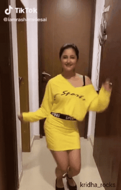 A Woman In A Yellow Sweater And Skirt Is Dancing GIF