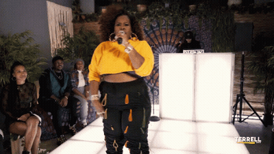 A Woman In A Yellow Sweater Sings Into A Microphone In Front Of A Dj Booth That Says Terrell On It GIF
