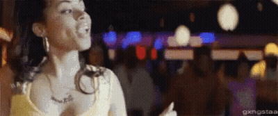 A Woman In A Yellow Tank Top Is Dancing In A Crowded Room . GIF