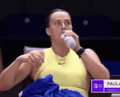 A Woman In A Yellow Tank Top Is Drinking Water From A Bottle . GIF