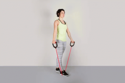 A Woman In A Yellow Tank Top Is Holding A Red Resistance Band GIF