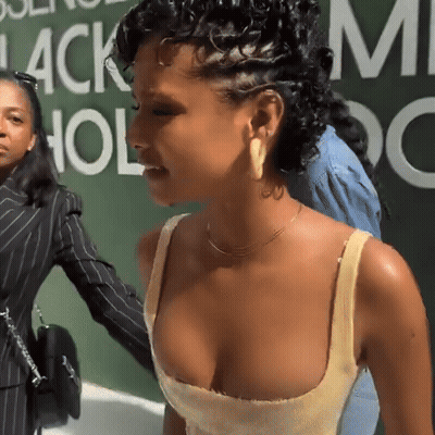 A Woman In A Yellow Tank Top Stands In Front Of A Green Wall That Says Black Hollywood GIF