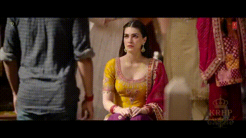 A Woman In A Yellow Top And Purple Pants Is Sitting In Front Of A Man In A Blue Shirt . GIF