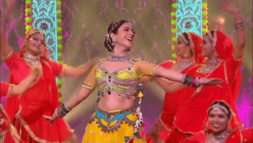 A Woman In A Yellow Top And Red Skirt Is Dancing With A Group Of Women In Red Dresses . GIF