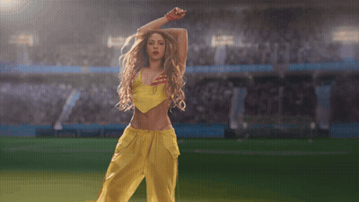 A Woman In A Yellow Top And Yellow Pants Is Dancing On A Soccer Field GIF