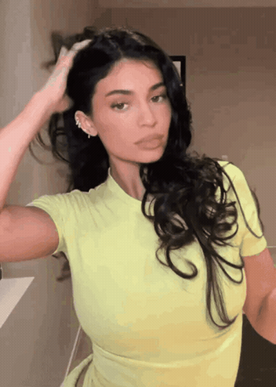 A Woman In A Yellow Top Is Holding Her Hair GIF