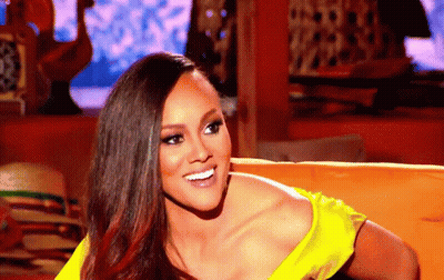 A Woman In A Yellow Top Smiles While Sitting On A Couch GIF