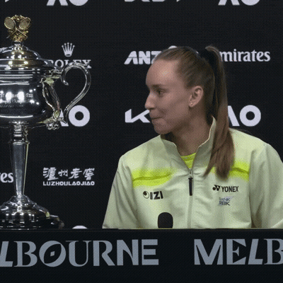 A Woman In A Yellow Yonex Jacket Stands In Front Of A Trophy At A Press Conference GIF