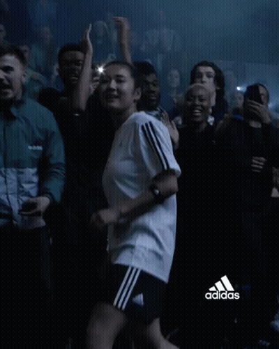 A Woman In An Adidas Shirt Is Dancing In A Crowd Of People GIF