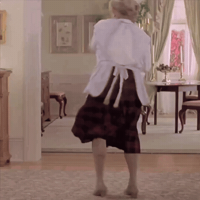 A Woman In An Apron Is Dancing In A Room GIF