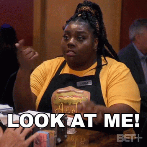 A Woman In An Apron Is Holding A Hot Dog And Says Look At Me . GIF