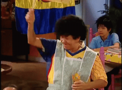 A Woman In An Apron Is Sitting At A Table With A Glass Of Orange Juice . GIF