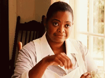 A Woman In An Apron Is Sitting In Front Of A Window And Smiling . GIF