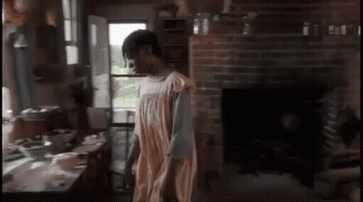 A Woman In An Apron Is Standing In A Kitchen GIF