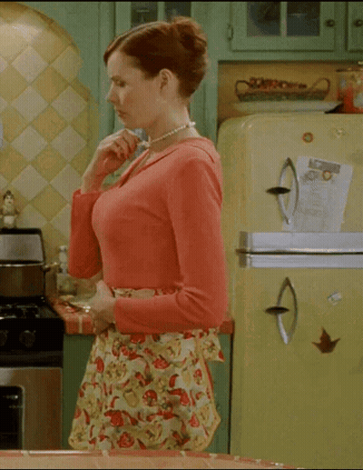 A Woman In An Apron Is Standing In A Kitchen With A Yellow Refrigerator GIF