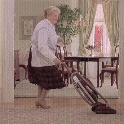 a woman in an apron is using a vacuum cleaner in a dining room