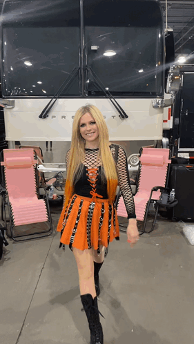 A Woman In An Orange And Black Dress Stands In Front Of A Camper GIF
