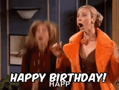 A Woman In An Orange Coat Is Standing Next To Another Woman In A Living Room . GIF