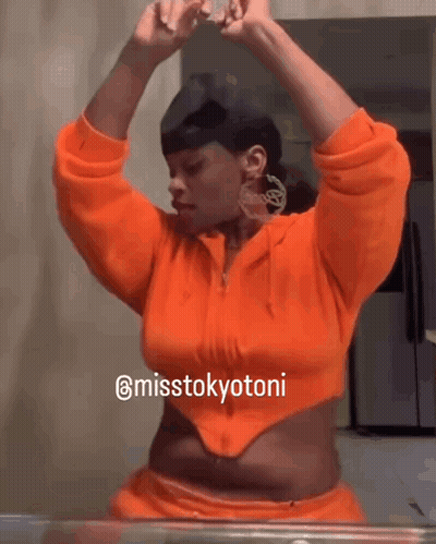 A Woman In An Orange Crop Top Is Looking At Herself In A Mirror GIF