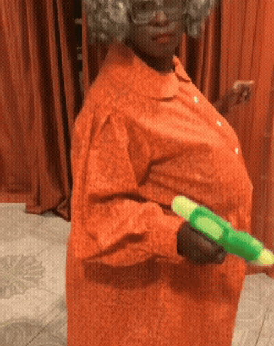 A Woman In An Orange Dress Is Holding A Green Toy Water Gun GIF