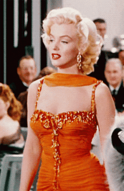 A Woman In An Orange Dress Is Standing In A Crowd GIF