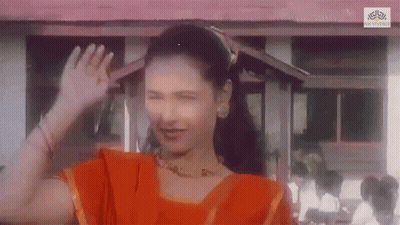 A Woman In An Orange Dress Is Waving Her Hand In Front Of A Building GIF