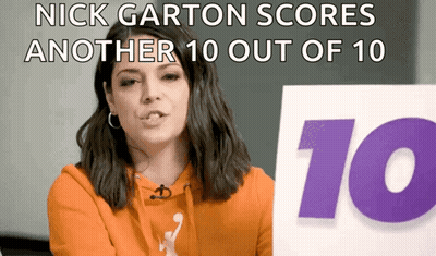 A Woman In An Orange Hoodie Holds Up A Sign That Says Nick Garton Scores Another 10 Out Of 10 GIF