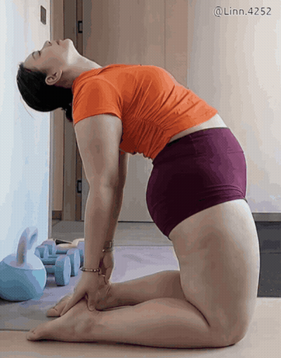 A Woman In An Orange Shirt And Purple Shorts Is Doing Yoga On A Mat GIF