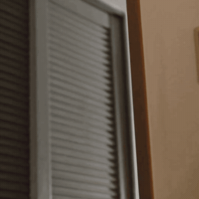A Woman In An Orange Shirt Is Peeking Out From Behind A Wall GIF