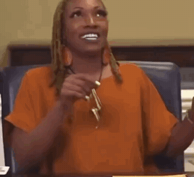 A Woman In An Orange Shirt Is Sitting At A Table Holding A Pair Of Earrings . GIF