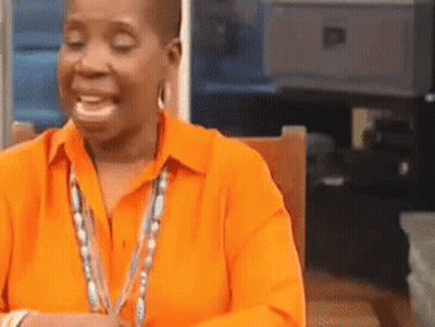 A Woman In An Orange Shirt Is Smiling And Sitting In A Chair . GIF