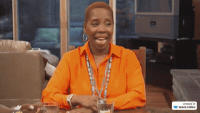 A Woman In An Orange Shirt Sits At A Table With Two Glasses Of Water GIF